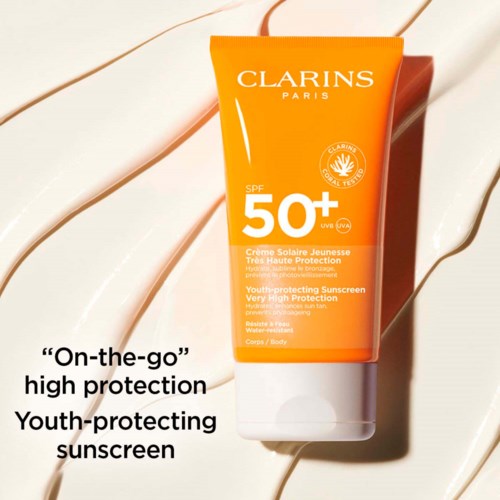 Oranje zonnescherm tube met SPF 50+, Clarins-merk en tekst over hoge bescherming en jeugdverzorging.