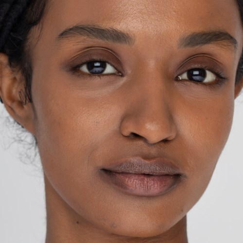 Een close-up van een vrouw met een gladde huid, donkere ogen en volle lippen, die recht in de camera kijkt.