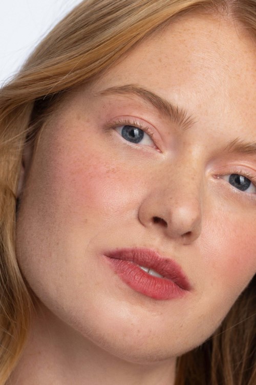 Close-up van een jonge vrouw met lichte huid, rood haar, lichte make-up en blauwe ogen.
