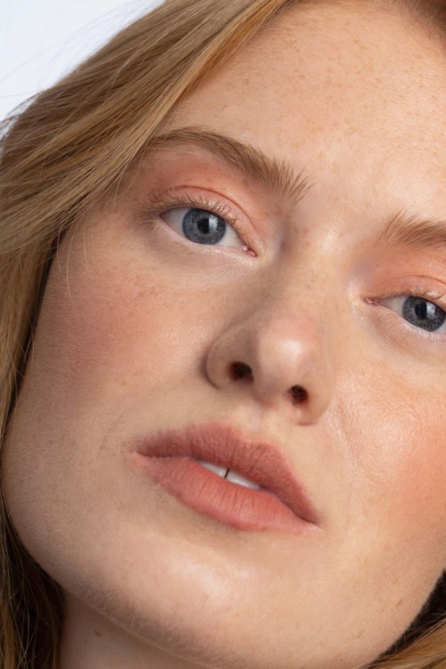 Een close-up van een jonge vrouw met lichte huid, rood haar, blauwe ogen en lichte make-up.