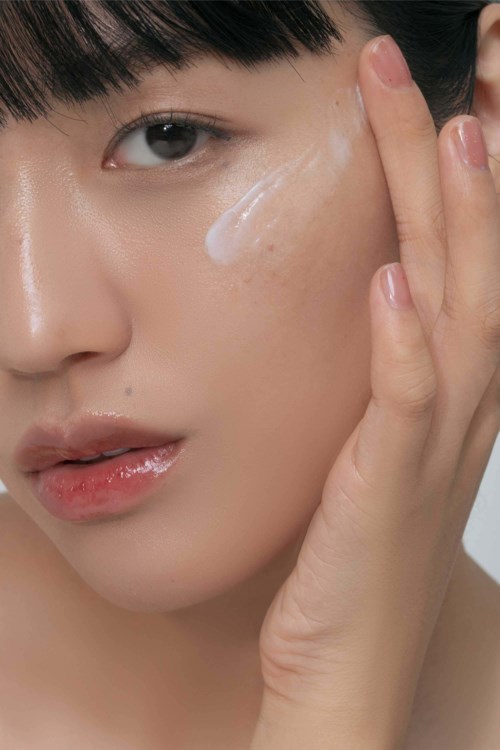Een vrouw brengt crème aan of raakt haar gezicht aan, met zichtbare lotion op haar wang, close-up.