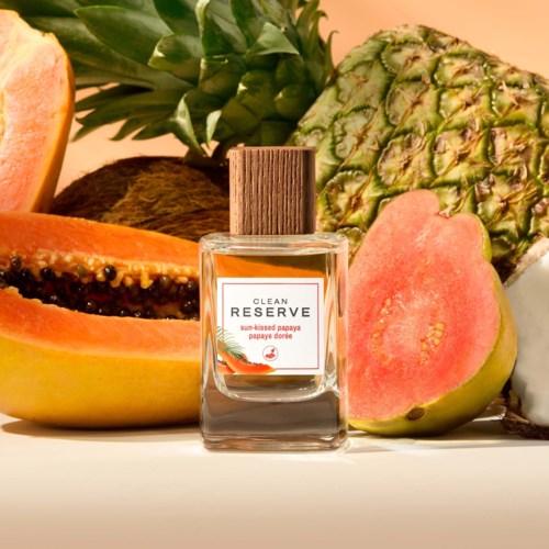 En parfymflaska märkt Clean Reserve omgiven av papaya, ananas och andra tropiska frukter.