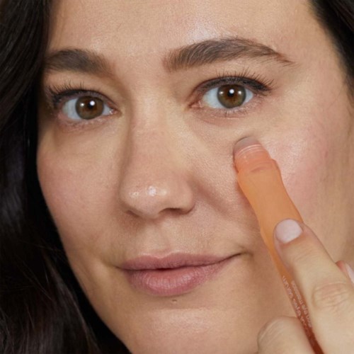 En kvinna använder en orange hudvårdsprodukt eller apparat nära sitt öga.