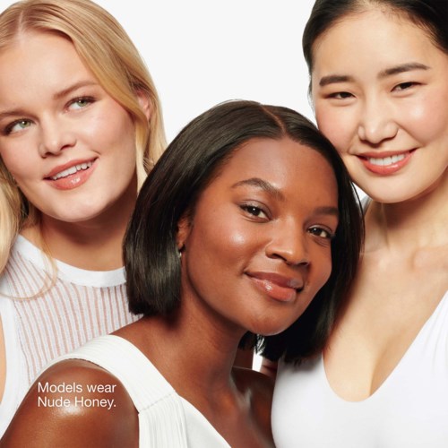 Drie vrouwen glimlachen, dragen witte kleren. Eén heeft een donkere huid, de anderen zijn licht. Tekst zegt dat ze Nude Honey dragen.