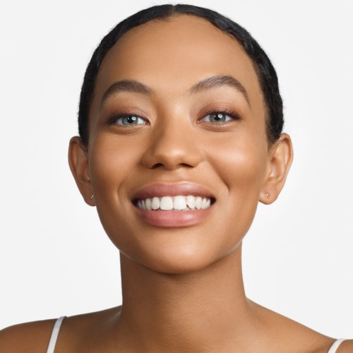 A smiling woman with clear skin, short dark hair, and blue eyes, wearing a white top against a plain background.