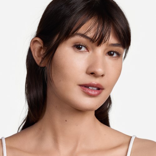 A woman with brown hair and bangs, wearing a white top, looks slightly to her right with a soft smile.