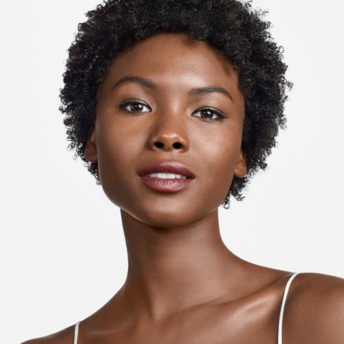 A woman with short curly hair, dark skin, and a confident expression. She wears a white strap top.