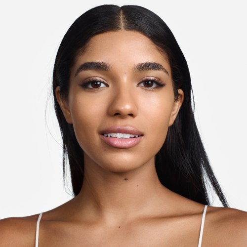 Een jonge vrouw met lang, zwart haar, lichte make-up en een zachte glimlach, draagt een witte top.