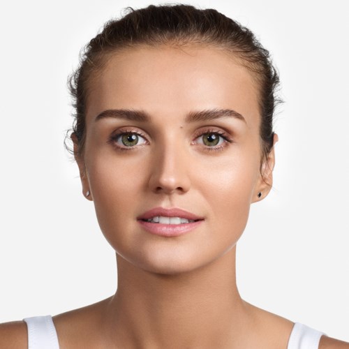 Een jonge vrouw met een heldere huid, lichte make-up en haar naar achteren, kijkt recht in de camera met een zachte glimlach.
