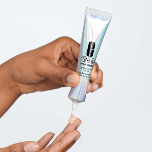 Een hand die crème uit een Clinique-tube knijpt, met crème die eruit komt, tegen een lichte achtergrond.