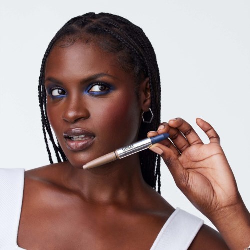 Een vrouw met gevlochten haar en opvallende make-up houdt een pen dicht bij haar gezicht en ziet er zelfverzekerd en stijlvol uit.