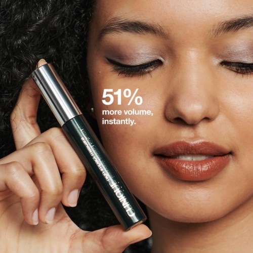 Vrouw houdt een mascara vast met de tekst: '51% meer volume, direct.' Ze heeft make-up op en haar ogen gesloten.