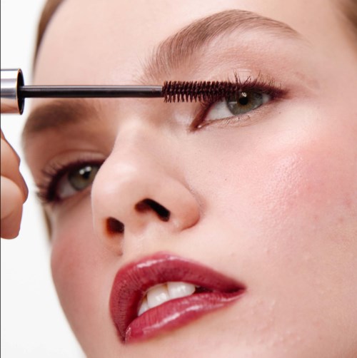 En kvinna applicerar mascara på ögat. Hon har ljus hud och blont hår. Fokus ligger på ögat och makeupen.