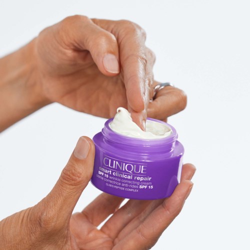 Iemand brengt crème aan uit een paarse potje van Clinique op de huid.