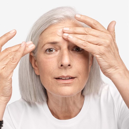 An older woman with gray hair touching her forehead and temple, looking concerned or thinking.