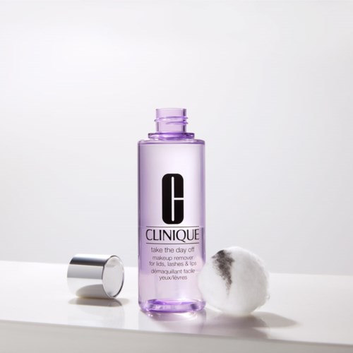 En Clinique makeup remover flaska med en bomullstuss bredvid på en vit yta.
