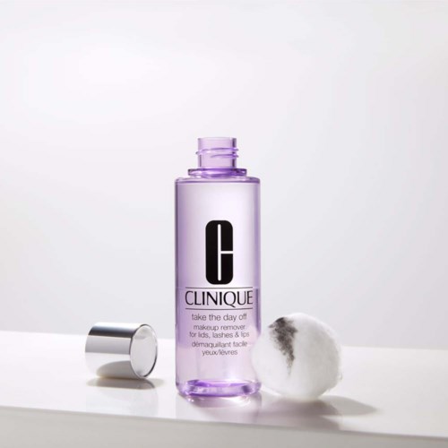 A Clinique makeup remover bottle with a cotton pad beside it, set on a white surface.