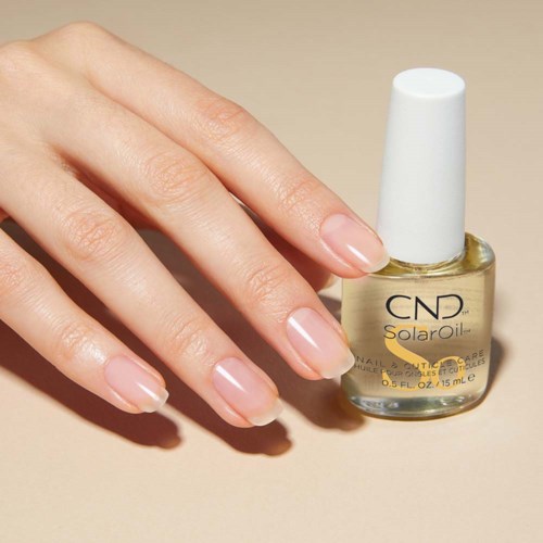 Eine Hand mit gepflegten Nägeln neben einer Flasche CND SolarOil für Nägel und Nagelpflegen.