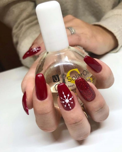 Eine Hand mit verzierter Nagel hält einen Nagellackflasche mit weißem Deckel. Die Nägel sind rot und glitzernd.