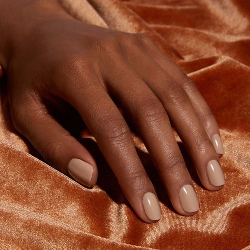 Eine Hand mit gepflegten beigen Nägeln liegt auf glänzendem, orange-braunem Stoff.