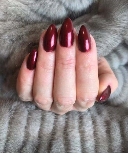 Eine Hand mit glänzenden dunkelroten Nägeln liegt auf einer grauen pelzigen Oberfläche.