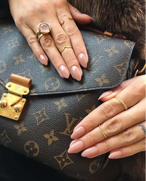Hände mit Ringen ruhen auf einer Louis Vuitton-Tasche mit goldener Hardware und Monogramm-Design.