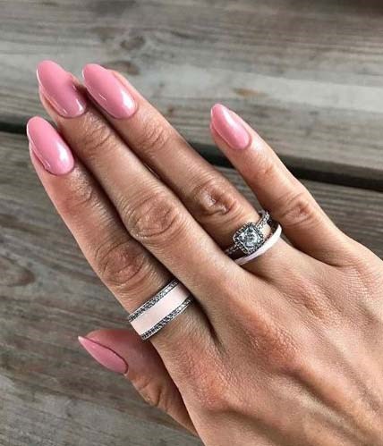 Eine Hand mit rosa Nägeln, einem Ring mit einem großen Edelstein und einem Silberband auf einer Holzoberfläche.