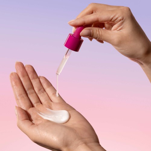 Een persoon gebruikt een roze pipet om vloeistof op hand te druppelen. De achtergrond is lichtpaars.