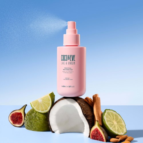 A pink spray bottle labeled 'COCO&EVE' stands on coconut, lime, fig, cinnamon, and almond slices against a blue sky background.