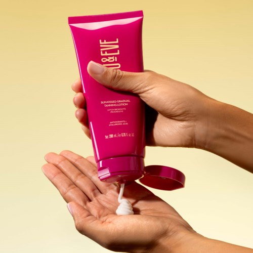 En hånd som presser ut brun-utan-sol-lotion på en annen hånd, med en beige bakgrunn.