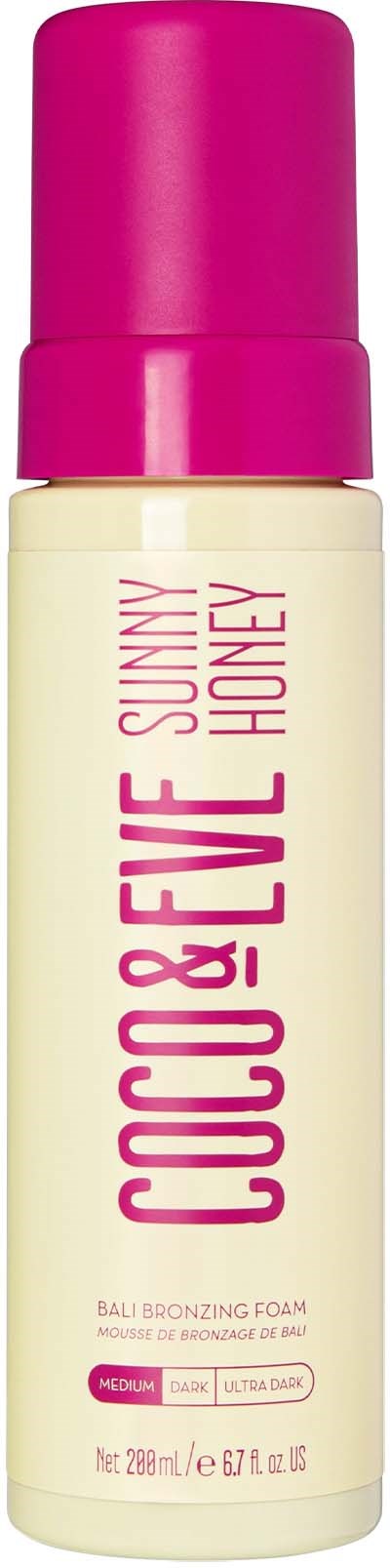 En flaske med Coco & Eve Sunny Honey Bali Bronzing Foam, med rosa hette og hvit kropp, viser produktnavn og detaljer.