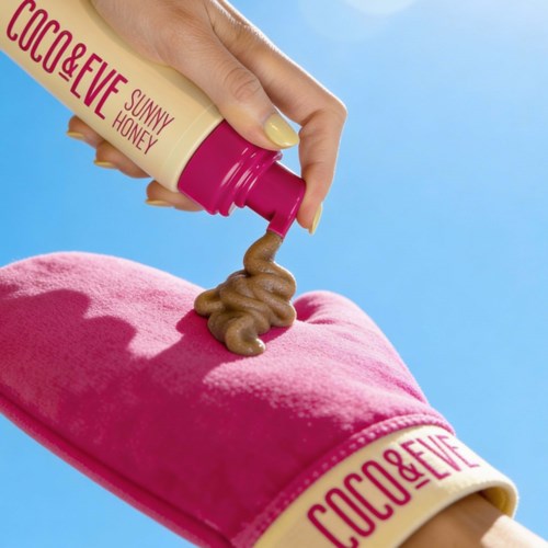 A person wearing pink oven mitts pours chocolate sauce onto a pink cake with a blue background.