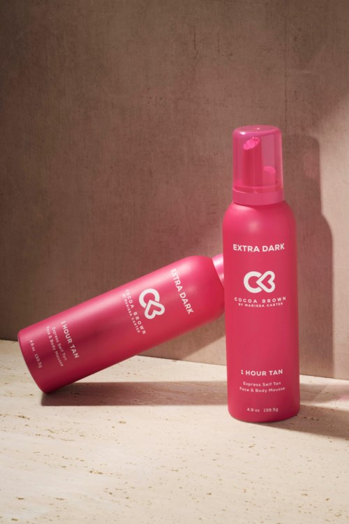 Zwei pinke Flaschen Selbstbräuner, gekennzeichnet 'Extra Dark' und '1 Hour Tan', stehen vor einem beigen Hintergrund.