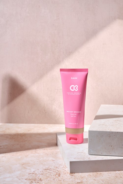 Eine pinke Tube mit Hautpflege- oder Schönheitsprodukt auf einer weißen Plattform vor schlichtem Hintergrund.