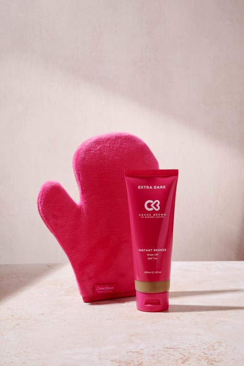 Ein rosa Ofenhandschuh neben einer roten Tube Bräunungscreme auf einer hellen Oberfläche.