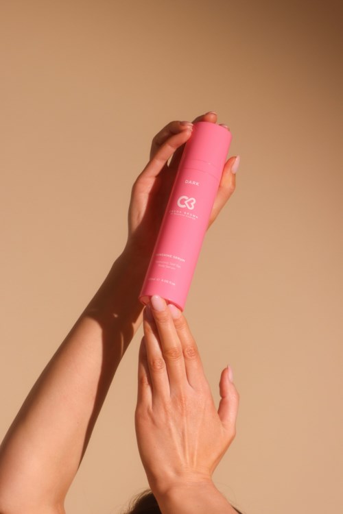 Eine Person hält eine pinke Flasche mit neutralem Hintergrund. Die Flasche hat weißen Text und ein Herzsymbol.