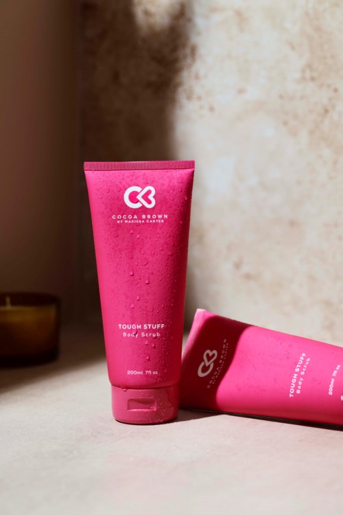 Zwei pinke Flaschen mit Cocoa Brown Hautpflegeprodukten auf einer Oberfläche, eine stehend und die andere liegend.