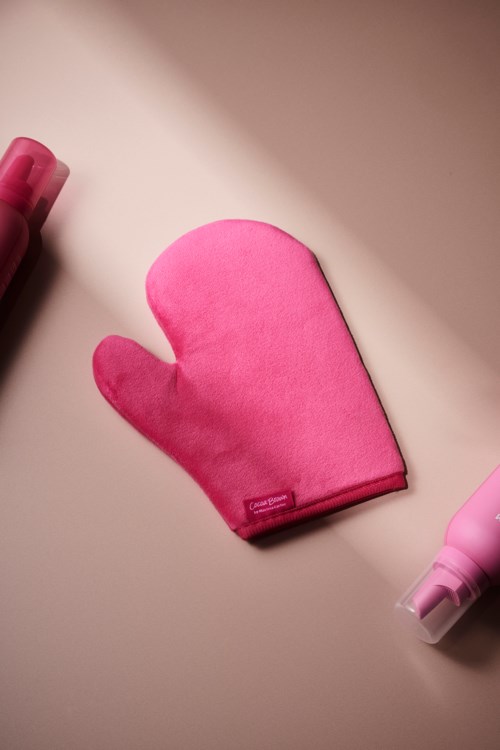 Eine rosa Ofenhandschuh, eine rosa Sprühflasche und eine rosa Flasche auf einer hellen Oberfläche.