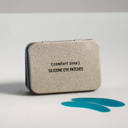 Eine kleine graue Blechdose mit der Beschriftung comfort zone Silikon Augenpads, mit zwei blauen Pads davor.