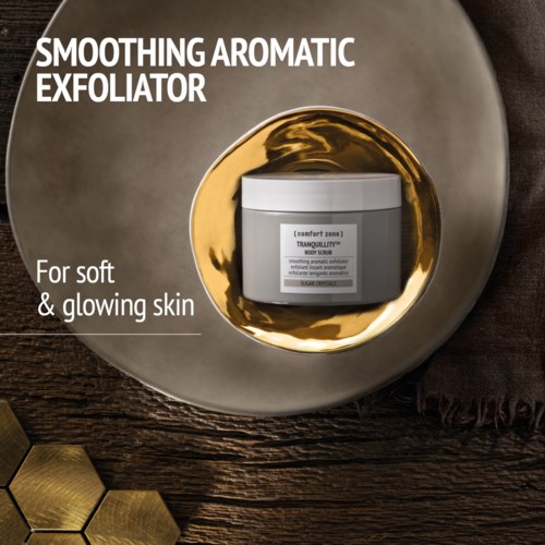 A skincare product called Smoothing Aromatic Exfoliator designed for soft, glowing skin, shown in a white jar on a decorative plate.