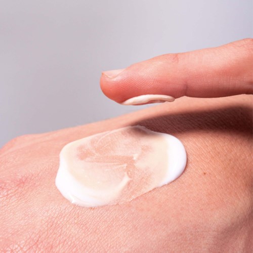 A person applies white cream to their skin with a finger on a light background.