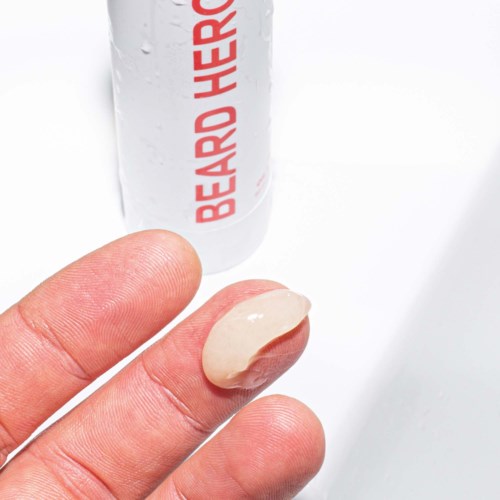 A finger with a large dollop of beige cream or lotion. A can with red text in the background. The setting is bright and white.