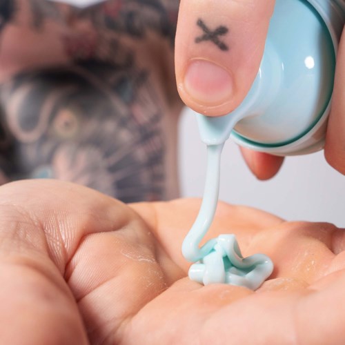 A person is squeezing white cream from a tube onto their hand.