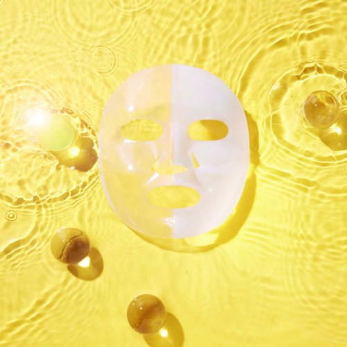 Eine weiße Gesichtsmaske schwimmt auf gelbem Wasser, mit einigen kleinen runden Gegenständen in der Nähe, die Sonnenlicht reflektieren.