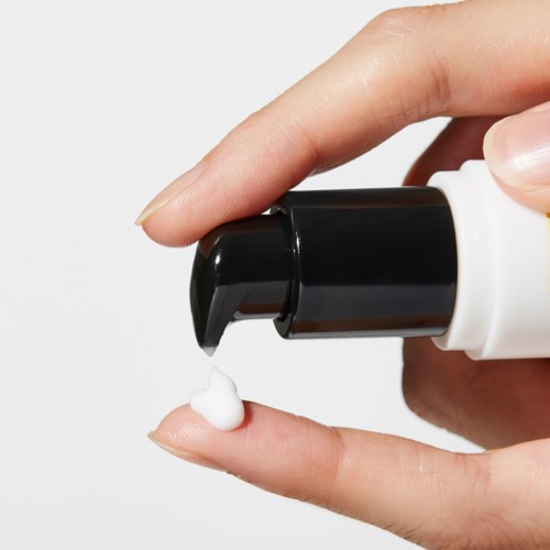 A hand pressing a pump to spray white cream onto a finger.