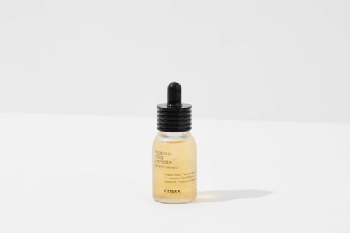 Eine kleine gelbe Flasche mit schwarzem Tropfenzähler, beschriftet 'Cosrx' auf weißer Oberfläche.