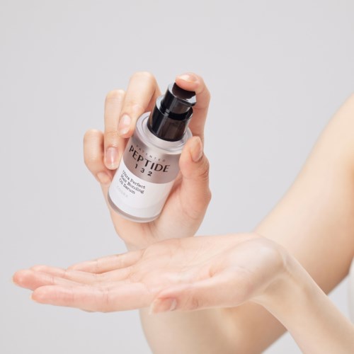 Een hand houdt een kleine fles met opdruk 'PEPTIDE 132', wat wijst op huidverzorging of cosmetica.