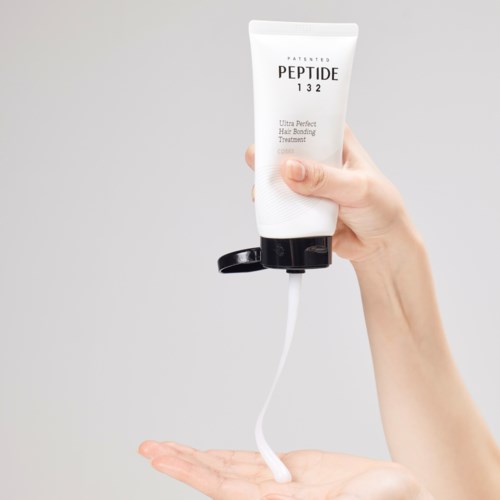Een hand knijpt een tube haarverzorging, het product stroomt eruit.