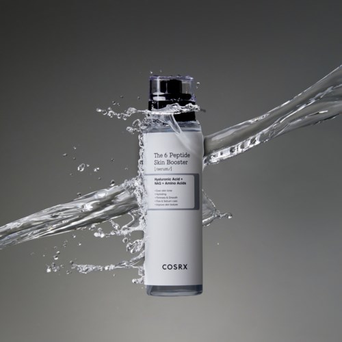 Eine weiße Flasche mit dem Aufdruck 'The 6 Peptide Skin Booster' und Wasser spritzt darum herum, vor grauem Hintergrund.