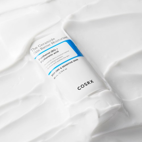 Een witte tube met COSRX label, ligt op een getextureerd witte oppervlak.